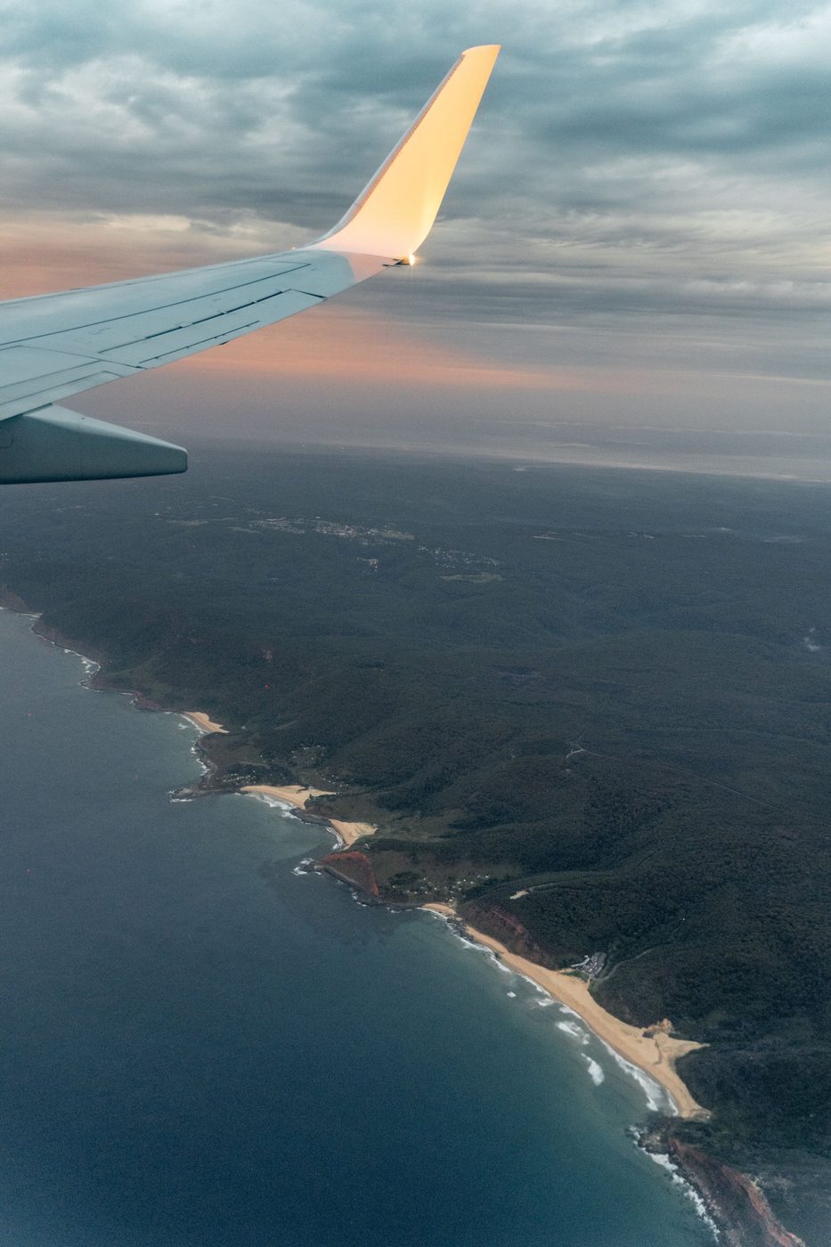 Vista da asa de um avião sobre o litoral ao entardecer